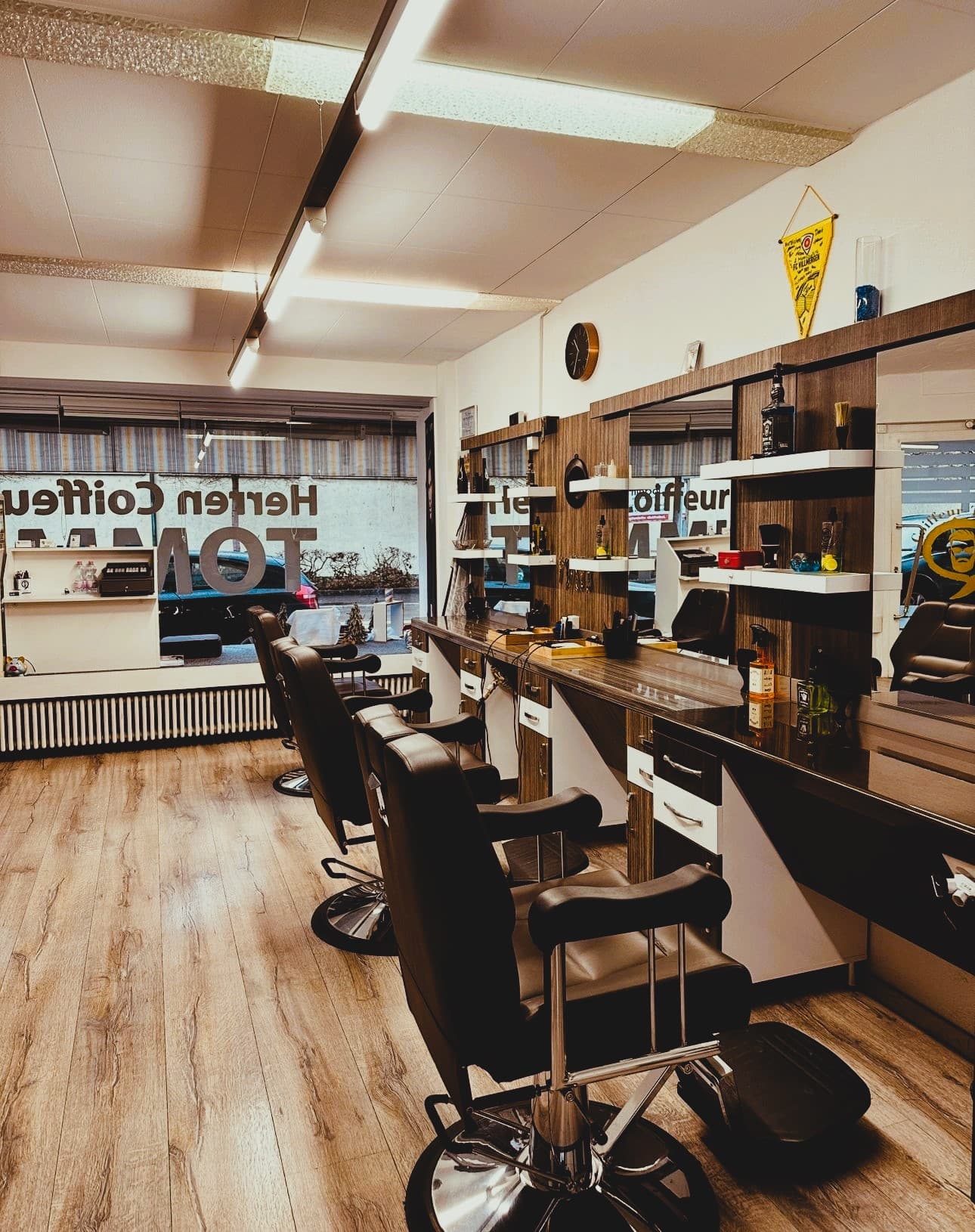 Salon von Coiffeur Tommi in Villmergen: Reihe schwarzer Barbierstühle vor Spiegeln und Holzregalen